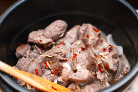 Meat with dried vegetables cooking in a deep metal pot or pan.の写真素材