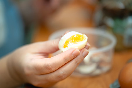 Woman holding a soft-boiled egg, bitten in half during a healthy breakfast.
