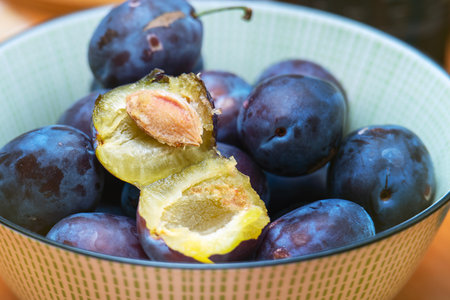 Plums in a bowl with one fruit halved, revealing green flesh and stone.の写真素材