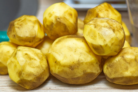 Peeled but unwashed potatoes lying on a kitchen table before cooking.の写真素材