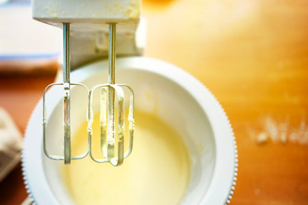 Mixer whisks raised over bowl with dough traces after finishing baking preparation.