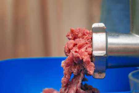 Side view of juicy red meat mince emerging from a meat grinder during processing.の写真素材