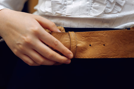 Girl in white blouse and black skirt fastening wide yellow eco-leather belt.の写真素材