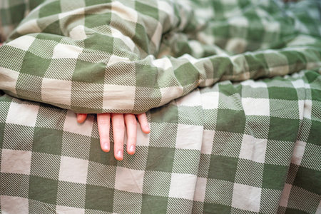 Teenager's fingers slightly peeking out from under a warm green plaid wool blanket. Cozy rest and...