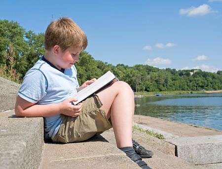 A little boy reads a big book with river at backgroundの写真素材