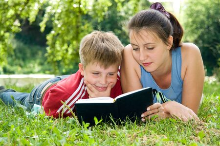 Mum and the son reads the book on a lawn in parkの写真素材