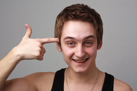 Give the screw-loose sign. Smiling young man on a grey backgroundの写真素材