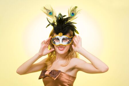 Portrait of a young woman wearing a carnival mask, on a yellow backgroundの写真素材