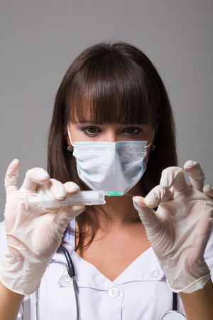 Young doctor wearing a mask with syringe on a grey backgroundの写真素材