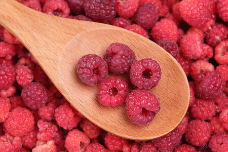 Red raspberries in a wooden spoon on red raspberries background. Close-up.の写真素材