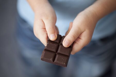 Broken piece of dark chocolate in child's hands.の写真素材