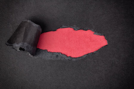 Red paper background appearing behind torn black paper.の写真素材