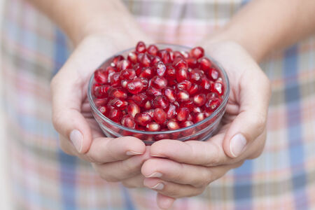 Pomegranate seeds in a bowl in woman's hands.の写真素材
