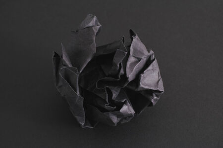 Crumpled black paper ball on a black background.