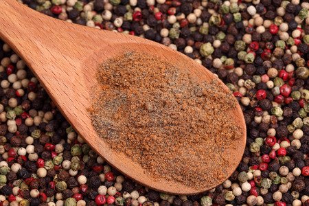 Ground mixed pepper in a wooden on a mixed peppercorn background. Close-up.