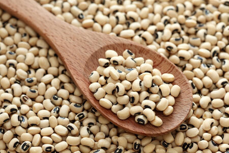 Black eyed peas in a wooden spoon on a black eyed peas background. Close-up.