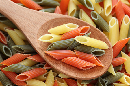 Penne rigate pasta in a wooden spoon on penne rigate pasta background. Close-up.の写真素材