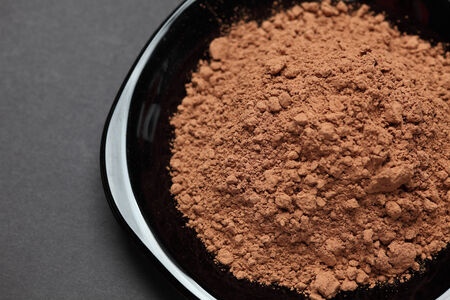 Heap of cocoa powder on a black plate on black background. Close-up.