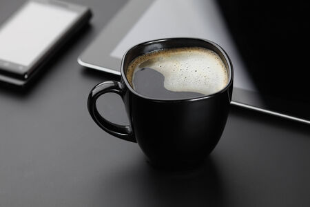 Black coffee in a black cup , black smartphone and black digital tablet on a black desk.の写真素材