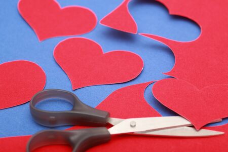 Hearts shape cut from red velvet paper on blue velvet surface with scissors . Close-up.の写真素材