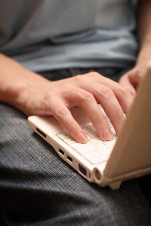 Young man using laptop on his lap. Focus on hands. Close-up.