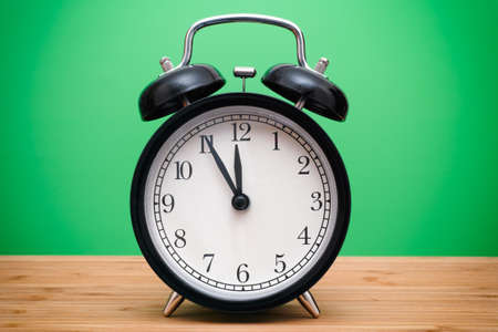 Black alarm clock against green background. Closeup. Vignette.