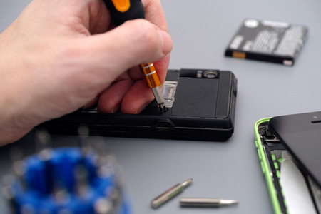 Man repairing cellphone with screwdriver. Cellphones have dust, dirt and  
scratches.の写真素材