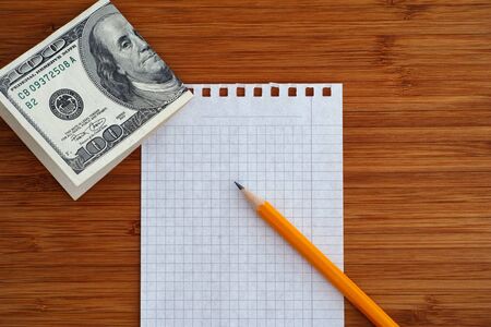 Blank sheet of paper and pencil with one hundred dollars bill on a wooden background. Close up.