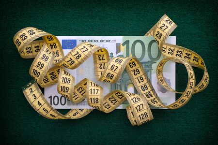 Measuring tape over one hundred euro note on green background. Close up.