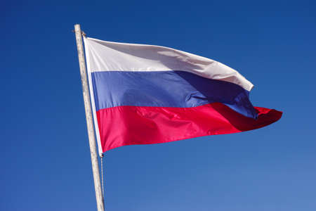 Russian National Flag waving in the wind against blue sky.