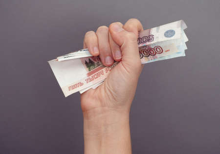 Woman hand squeezes russian money against grey background.の写真素材