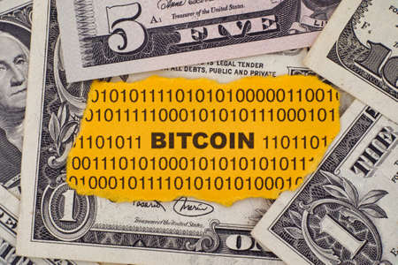 Piece of paper with the word Bitcoin on dollar bills. Close up.