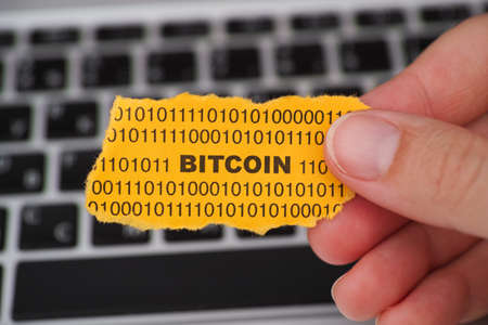 Woman holds yellow piece of paper with the word Bitcoin against computer keyboard.の写真素材