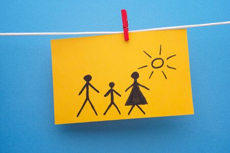 Drawing of a family on yellow piece of paper. Blue background. Close up.の写真素材