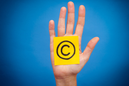 Yellow paper note with Copyright symbol in woman palm. Blue background.の写真素材