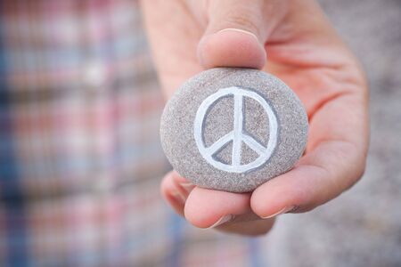 Person holds stone with peace symbol. Close up.
