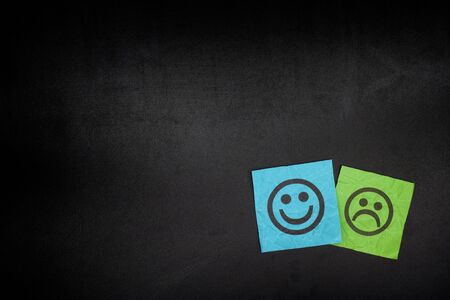 Blue and green paper notes with happy and sad faces on blackboard. Vignette.の写真素材
