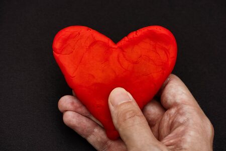 A man holding a red heart in his hands. Black background. Close up.の写真素材