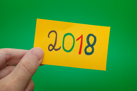 Person holding yellow paper note with 2018 year written on it. Green background.の写真素材