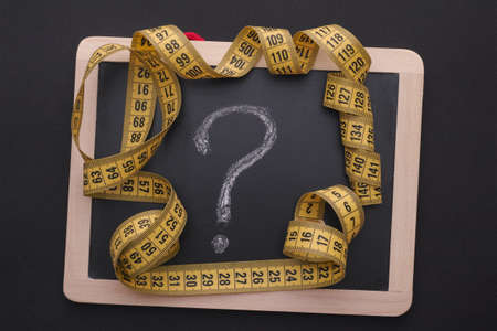 Measuring tape on blackboard with question mark. Black background.の写真素材