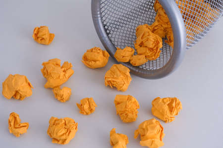 Yellow crumpled paper balls rolling out of a trash can. Idea Concept.