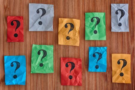 Colorful paper notes with question marks on a wooden background. Concept image.