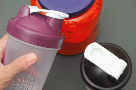 Person holds empty shaker in his hand above protein jar. Close up.の写真素材
