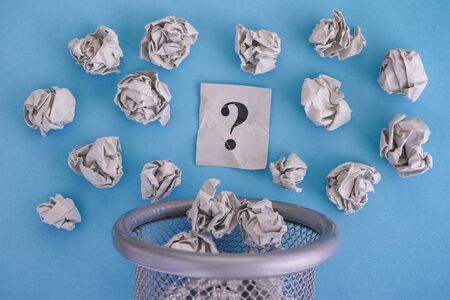 Gray crumpled paper balls and question mark rolling out of a trash can. Close up.