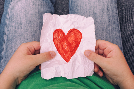 Young boy holding crumpled piece of paper with red heart shape. Close up.の写真素材