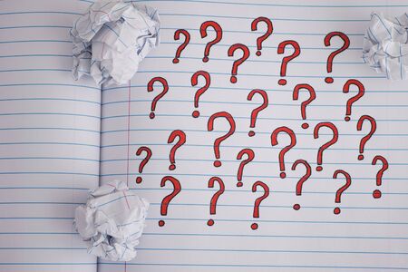 Question marks on notebook sheet with some crumpled paper balls on it. Close up.の写真素材