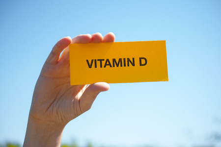 Hand holds piece of paper with Vitamin D against sunny blue sky. Close up.の写真素材
