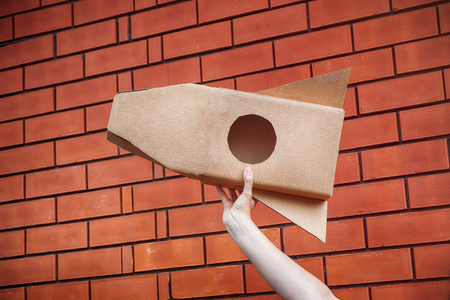 Cardboard space rocket in hand against brick wall. Concept image.の写真素材