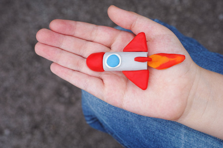 Young boy holds a space rocket in his hand. Close up. Space rocket is made out of plasticine.の写真素材