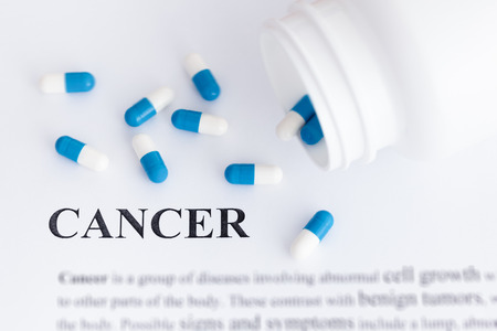 Word Cancer on paper with pills spilling out of a bottle. Close up.の写真素材